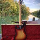 Elektrická basová kytara s tělem v provedení sunburst a světlým hřidlem. Na hlavě je viditelné logo Fender. Nástroj je umístěn v otevřeném kufru s če…