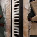 Černý digitální klavír s bílými a černými klávesami. Na pravé straně korpusu je viditelný nápis YAMAHA. Nástroj leží na dřevěném povrchu a je částečn…