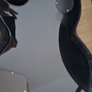 Černá kytara s lesklým povrchem v otevřeném kufru. Na zadní straně těla jsou vidět dvě černé plastové krytky připevněné šrouby. Povrch nástroje je hl…