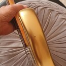 Detailní pohled na hranu těla elektrické kytary v zlatém lesklém laku. Na povrchu laku je viditelný malý tmavý škrábanec nebo oděr. Na fotce nejsou ž…