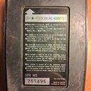 Fotografie zachycuje zadní stranu černého efektového pedálu s nalepeným informativním štítkem. Na štítku je nápis DC9V AC ADAPTER a texty v několika…