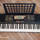 Černý elektronický klavír značky YAMAHA s modelem PSR-220. Nástroj má bílé a černé klávesy, nad nimi se nachází ovládací panel s displejem a řadou tl…
