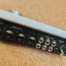 Zadávací panel černého elektronického zařízení se stříbrným horním krytem. Panel obsahuje čtyři vstupy označené ANALOG IN (1–4), pět výstupů ANALOG O…