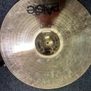 Zlatý kovový činel s viditelným broušením povrchu. Na horní části je černý nápis PAiste a nad ním menší text MADE IN SWITZERLAND. Povrch je v dobrém…