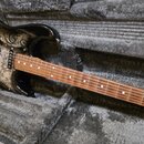 Elektrická kytara v černém lakovaném těle s ornamentálním vzorem paisley. Na hlavě hředu je viditelné logo Fender. Hmatník je vyroben z tmavého dřeva…