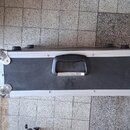 Černý transportní kufr s hliníkovým rámem a kovovými rohy. Uprostřed je umístěna černá plastová rukojeť s kovovým úchopem. Na povrchu nejsou viditeln…