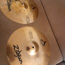 Dvě mosazné činely značky Zildjian. Oba mají nápis CUSTOM a logo ve tvaru písmena A. Spodní činel má v dolní části drobný nečitelný text a technické…