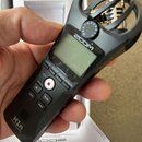 Černý digitální diktafon s integrovaným mikrofonem v ochranném koši. Na horní části je bílý nápis ZOOM a ve spodní části označení H1n Handy Recorder.…