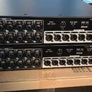 Dvě černé rackové jednotky značky YAMAHA s označením I/O RACK Tio1608-D. Každé zařízení má v horní části 16 vstupních konektorů INPUT a v dolní části…