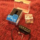 Na fotografii je černý kytarový snímač s nápisem Seymour Duncan. Součástí je průhledný plastový box s modrou krabičkou, na které je text Seymour Dunc…