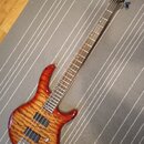Elektrická basová kytara s tělem z masivního dřeva s výraznou plamenovitou strukturou v červenohnaté barvě. Na hlavě je viditelné logo Ibanez a nápis…