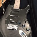 Černá elektrická kytara s jasným povrchem a černým pickguardem, položená v černém obalu. Nástroj má světle hnědý hmatník a tři humbuckery. Na ovládac…