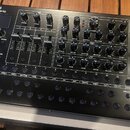 Černý syntetizátor s nápisem Roland SYNTHESIZER SH-01d. Přední panel obsahuje množství otočných knoflíků, posuvníků a tlačítek s bílými popisky sekcí…