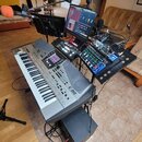 Sestava hudebního vybavení na stojanu. Dominantním prvkem je šedý klavír s nápisy Roland a E-80. Nad klavírem je umístěn monitor, mixovací pult s mod…