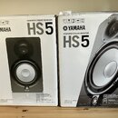 Dvě bílé krabice od studiových monitorů. Na obou je vidět logo YAMAHA a nápisy POWERED STUDIO MONITOR HS5. Na krabicích jsou fotografie černých repro…