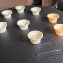 Deset plastových knoflíků v bílé a krémové barvě rozložených na černé povrchové ploše. Knoflíky mají válcový tvar s žebrovaným spodním okrajem a proh…