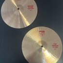 Dvě mosazné činely typu hi-hat. Horní činel má červený nápis MEDIUM HI-HAT BOTTOM 14" a logo PAIST. Dolní činel má červený nápis TOP MEDIUM HI-HAT 14…