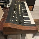 Černý elektronický klavír s dřevěným šasi. Na ovládacím panelu je nápis YAMAHA a řada posuvníků, tlačítek a dvou otočných potenciometrů s popisky OUT…