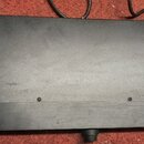 Fotografie zachycuje spodní stranu černého, obdélníkového elektronického zařízení. Povrch je matný s viditelnými škrábanci a prachem, v dolní části j…