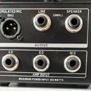 Černý elektronický přístroj s několika konektory. V horní části jsou výstupy OUTPUT označené jako EMULATED MIC (BAL) s XLR konektorem, LINE (UNBAL) a…