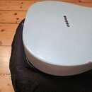 Bílá, zaoblená elektronická součást nebo zařízení s řadou pěti malých otvorů na horní straně. Předmět leží na černé látkové tašce nebo pouzdře, které…