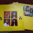 Žlutý obal vinylovové desky s tracklistem a fotografiemi čtyř členů kapely. Na obalu jsou vidět dvě černá radiační znamení a v levém horním rohu logo…