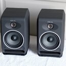 Dva šedé studiové reproduktory značky FOCAL. Každý má v horní části výškovek a ve spodní části basový reproduktor s bílým vnějším kroužkem. V dolní č…