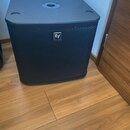 Černý subwoofer s mřížkou a horní plochou, která obsahuje otvor pro instalaci tyče. Na přední straně je umístěno bílé logo Ev. Povrch nástroje vykazu…