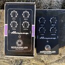 Černý efekt pedál Ampeg SCRAMBLER Bass Overdrive a jeho originální kartonová krabice. Pedál má čtyři otočné ovladače s nápisy Drive, Blend, Treble a…