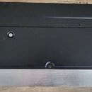 Fotografie zachycuje spodní stranu černého elektronického zařízení s kovovou stříbrnou lištou v dolní části. Na černém povrchu jsou vidět početné škr…