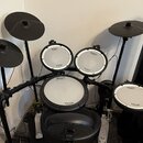 Elektronická bicí souprava značky Roland s černým rámem a gumovými pady. Na všech bubnových plochách je vidět nápis Roland V-Drums, přičemž na dvou h…