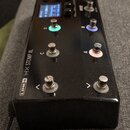 Černý efektový pedál s nápisem LINE 6 HX STOMP XL. Zařízení má pět kovových spínacích tlačítek, z nichž tři jsou podsvícená v zelené, modré a růžové…