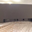 Detail zadní strany šedého elektronického zařízení s nápisem YAMAHA. Jsou vidět konektory: jeden hranatý port, jeden kulatý vícepinový konektor a dva…