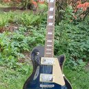 Tmavě modrá elektrická kytara s tvarem singlecut a krusem z tmavého dřeva. Na hlavě je bílý nápis Gibson a na těle jsou dva humbuckery s krémovými rá…