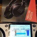 Fotografie zobrazuje krabici s černými sluchátky Pioneer DJ HDJ-X5 a část DJského kontroléru. Na krabici je nápis Pioneer DJ a model HDJ-X5 DJ Headph…