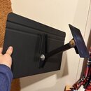 Černý kovový držák s dvěma plochými deskami, které jsou spojeny nastavitelním ramenem. Na povrchu kovových částí nejsou viditelné žádné značky ani ná…