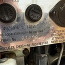 Detail kovového panelu s dvěma černými zátlačkami s nápisem FUSE. Na povrchu je text 40/60 Hz ∿ 175 W, this apparatus must be earthed a SERIAL No: 03…