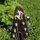 Hlava kytary z tmavého dřeva sáhlá k hornímu okraji. Na čele je bílý nápis „Kask GUITAR“. Jsou zde vidět šest chromovaných ladiček a struny. Povrch d…