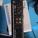 Zadní strana černého audio rozhraní s nápisy SSL 2+ a Solid State Logic. Jsou zde viditelné konektory USB, MIDI IN a OUT, dva výjemy PHONES, pět OUTP…