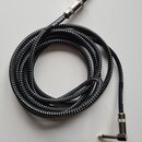 Černý instrumentální kabel s pleteným povrchem. Na jednom konci je rovný konektor a na druhém úhlový konektor, oba s kovovým povrchem. Na kabelu u ro…