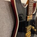 Detail elektrické kytary s černým bodies a červeným okrajem. Nástroj má zlatý hardware, včetně dvou humbuckerů a mostu. Na povrchu laku jsou viditeln…