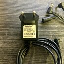 Černý síťový adaptér s evropskou vidlicí a připojeným kabelem. Na bílém štítku je uveden název RockPower Power Supply a model NO-RP NT 50 EU(G)121E-0…