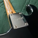 Detail spojení krku a těla černé kytary. Na kovovém krytu je vyryto logo Squier®. Povrch laku na těle je hladký a lesklý, kovový kryt je připevněn čt…