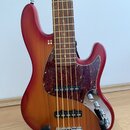 Čtyřstrunná elektrická basová kytara s červeným gradientním lakem a hnědým dřevěným povrchem. Nástroj má tmavý vzorovaný pickguard, dva snímače a tři…