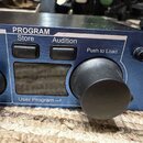 Detailní záběr na modrý kovový panel elektronického zařízení. Jsou zde vidět tlačítka s nápisy Store a Audition pod nadpisem PROGRAM, text Push to Lo…