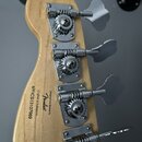 Zadní strana hlavy basové kytary z přírodního dřeva se čtyřmi chromovanými ladičkami. Na dřevě je černý nápis: Designed and Backed by Fender, Crafted…