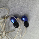 Modré špunty (in-ear monitory) s černými silikonovými nástavky a průhledným kabelem. Na obou sluchátkách je viditelný nápis SE846. Kabel končí zlatým…