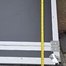 Fotografie zobrazuje šedý transportní kufr s hliníkovými hranami a kovovými rohy. Ruka drží žlutou skladovací metr, který měří délku kufrů. Na povrch…