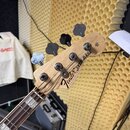 Hlava basové kytary z přírodního dřeva s nápisem Fender Jazz Bass. Na hlavě jsou čtyři kovové ladičky a v horní části je vyryto číslo 1331. Hřeben hm…