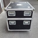 Dvě černé transportní bedny (flightcase) naskládané na sebe. Mají kovové hrany, rohy a čtyři zapadací zámky v přední části. Na horní bedně jsou vidět…